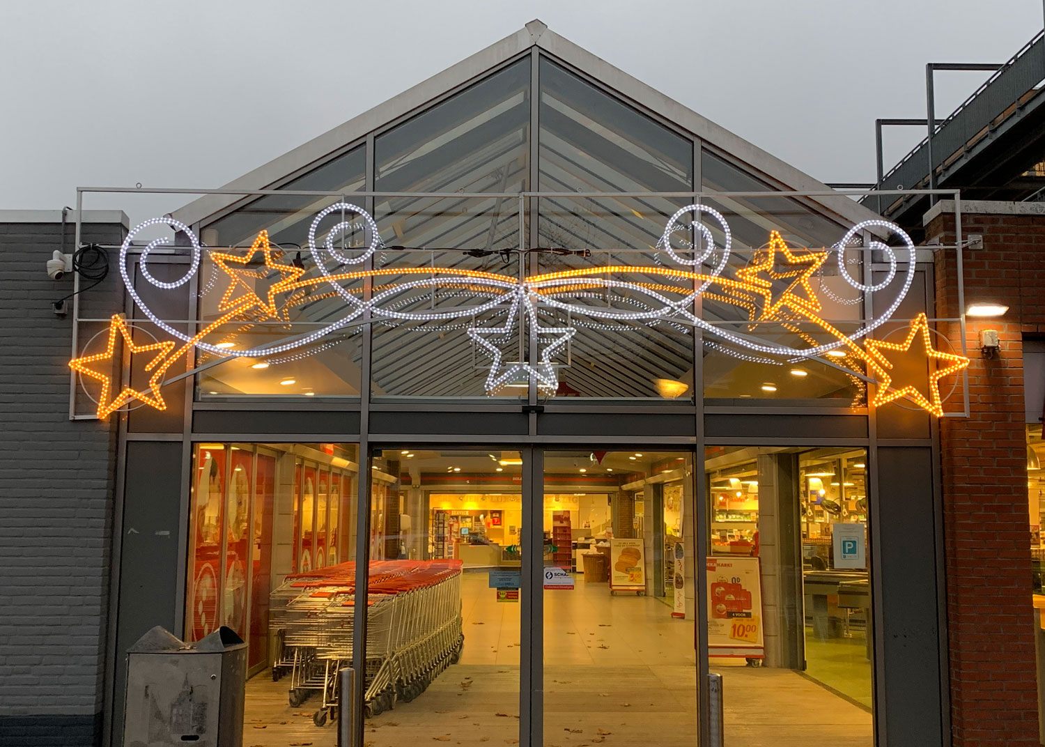 Entree van een supermarkt met gouden sterren en krullen in lichtslang boven de luifel