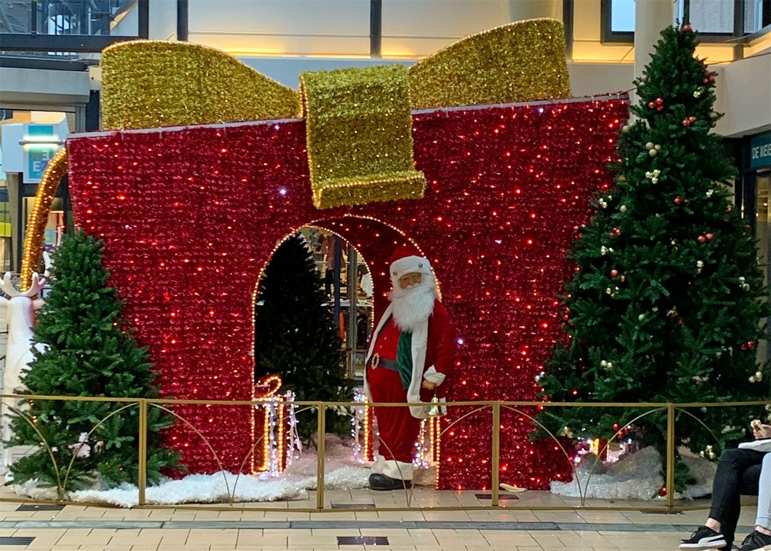 Groot rood cadeau met gouden strik en kerstman tussen kerstbomen