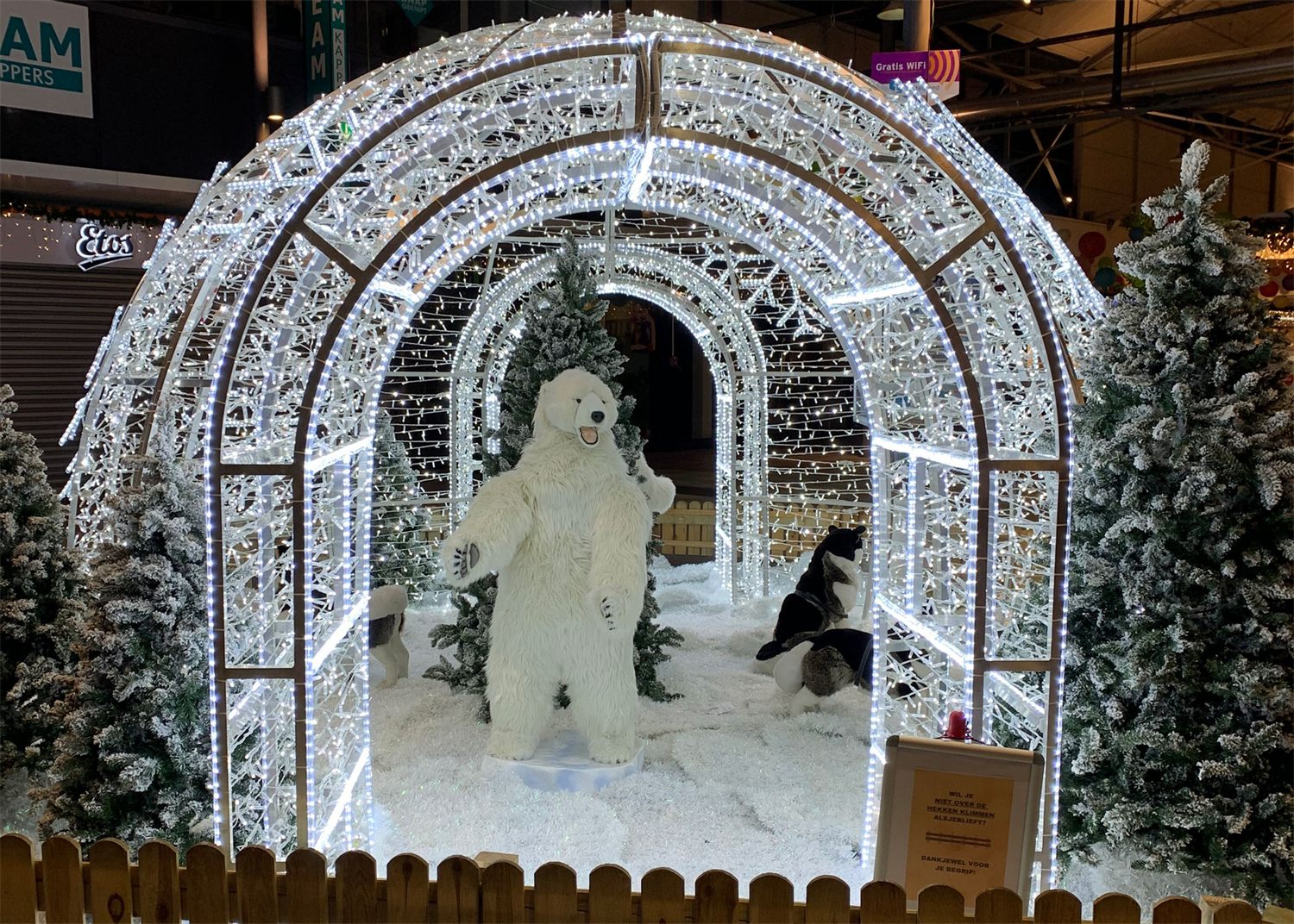 Verlichte iglo met ijsbeer en besneeuwde kerstbomen in een winkelcentrum