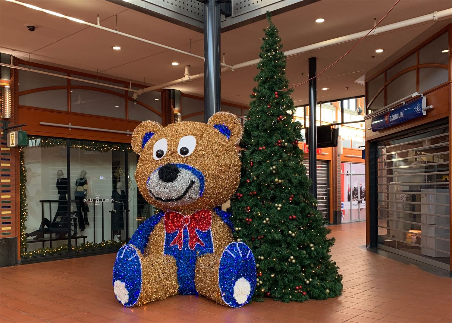 Grote bruine beer met blauwe sjaal naast een kerstboom