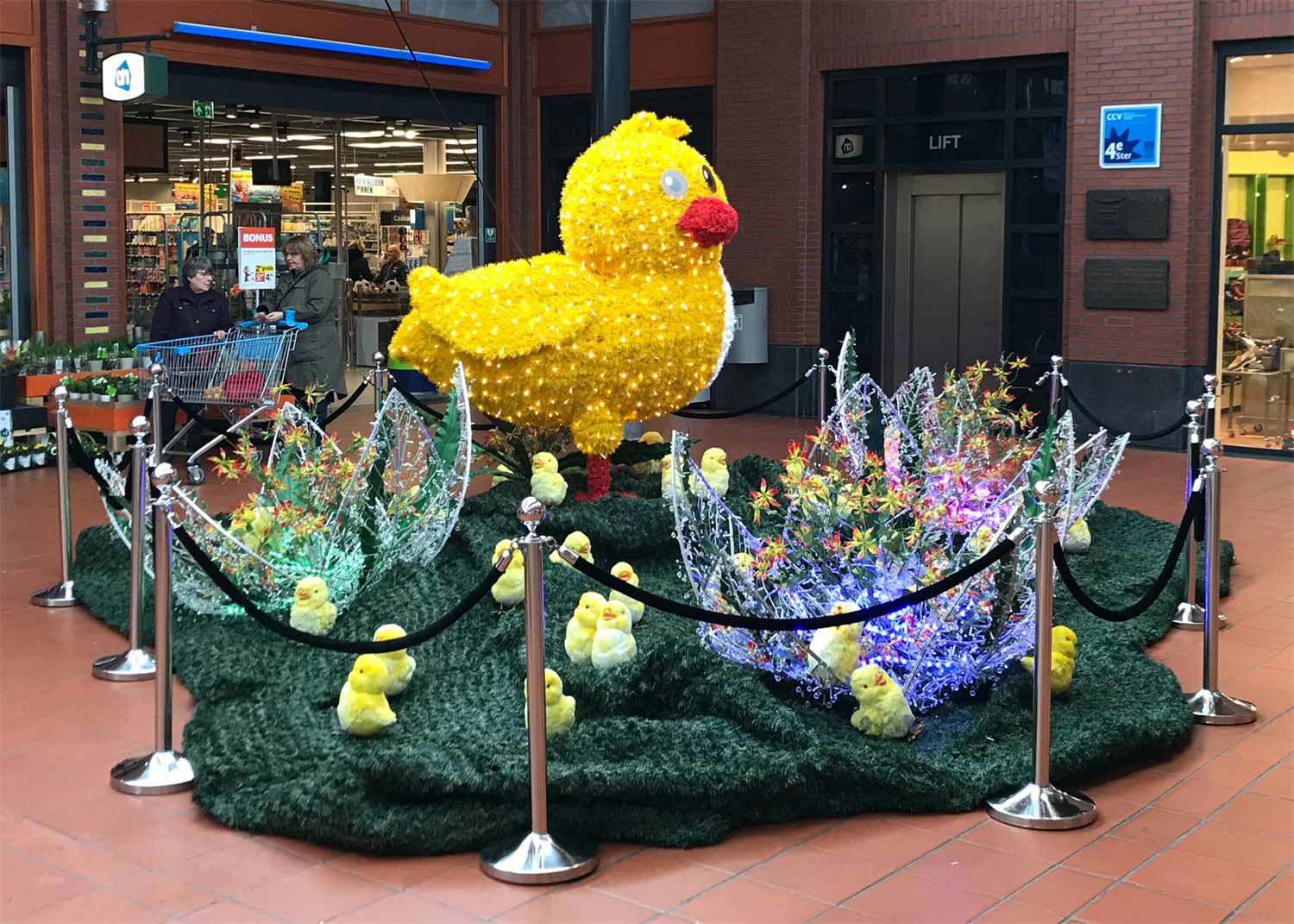 Verlicht geel paaskuiken op een veld met gekleurde bloemen in een winkelcentrum