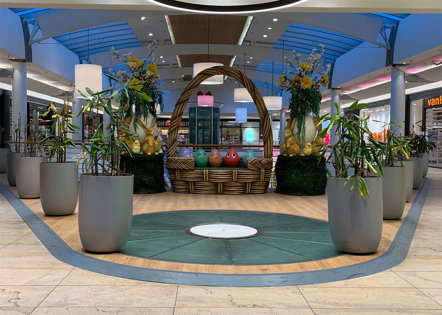 Reuzenpaasmand met voorjaarsbloemen tussen plantenbakken in een winkelcentrum