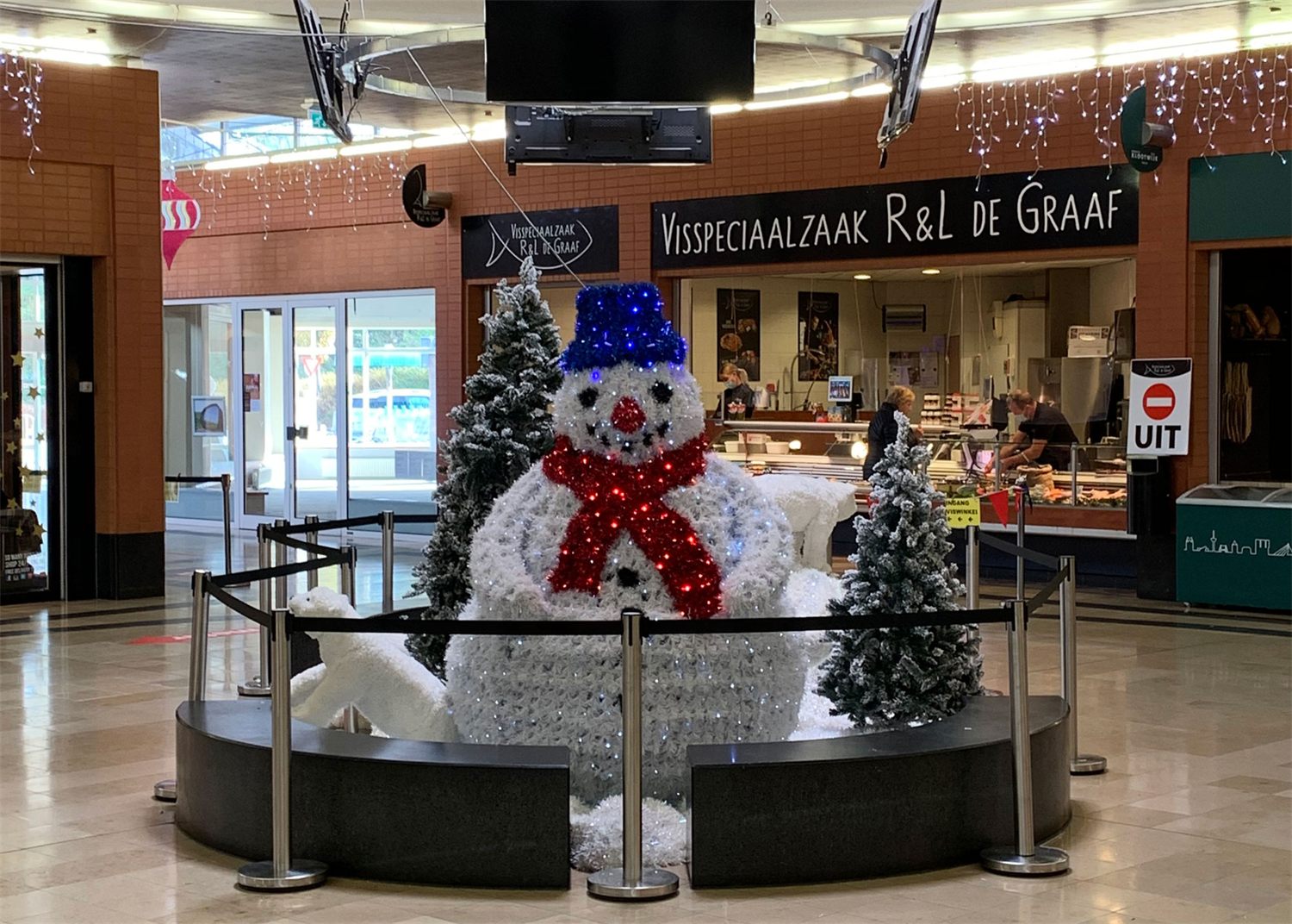 Sneeuwpop op een ronde sokkel met kunstsneeuw en kerstbomen in een winkelcentrum